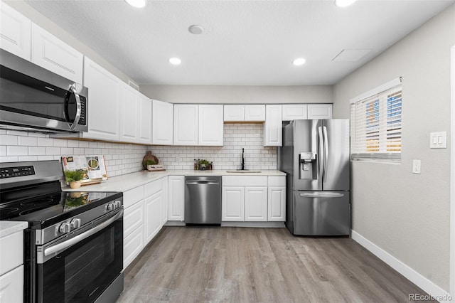 kitchen with stainless steel appliances, light countertops, backsplash, white cabinetry, and a sink