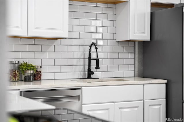 kitchen featuring light stone counters, a sink, white cabinetry, appliances with stainless steel finishes, and decorative backsplash