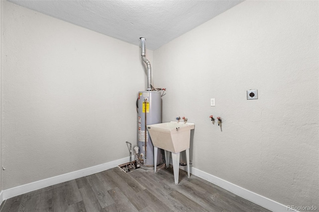 washroom with water heater, electric dryer hookup, wood finished floors, laundry area, and baseboards