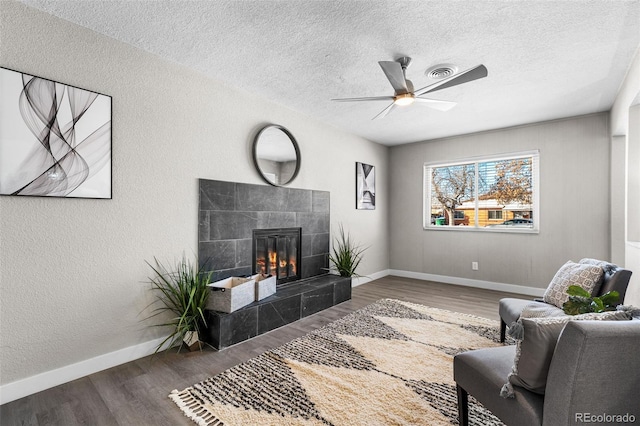 living room featuring a textured wall, visible vents, wood finished floors, and a tile fireplace