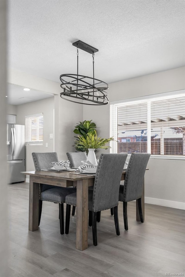 dining space with light wood-style floors, a textured ceiling, and baseboards