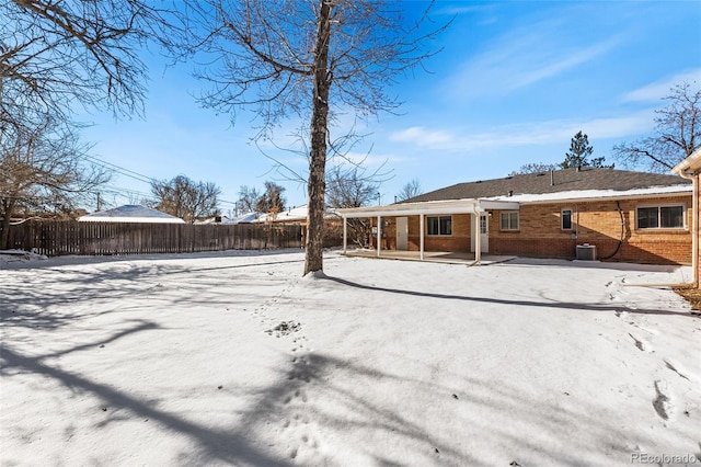 snow covered house featuring fence private yard, a patio area, brick siding, and central AC