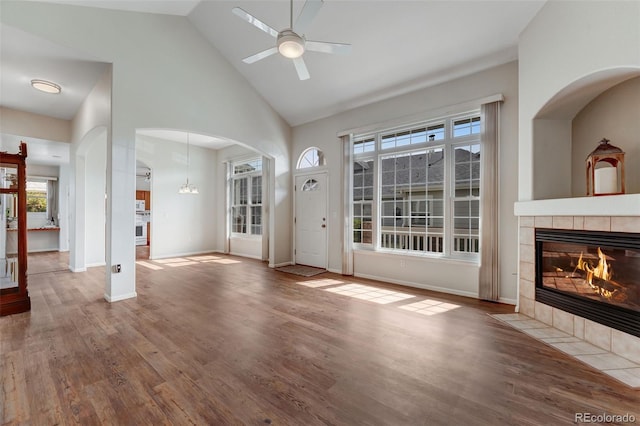 unfurnished living room featuring a fireplace, a ceiling fan, high vaulted ceiling, wood finished floors, and arched walkways