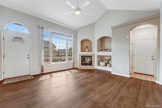 entryway with a ceiling fan, wood finished floors, a fireplace, high vaulted ceiling, and baseboards