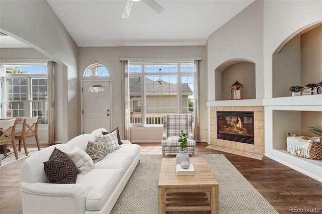 living area with wood finished floors, a tile fireplace, a ceiling fan, and baseboards