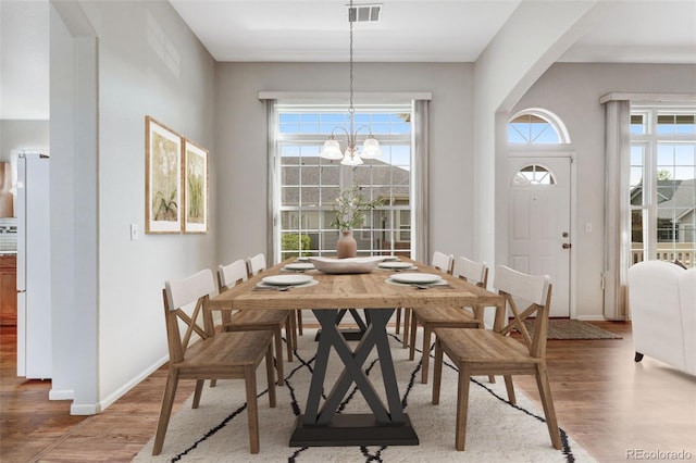 dining area with wood finished floors, a chandelier, arched walkways, and baseboards