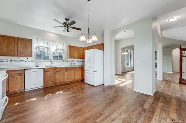 kitchen with a sink, white appliances, ceiling fan with notable chandelier, wood finished floors, and backsplash