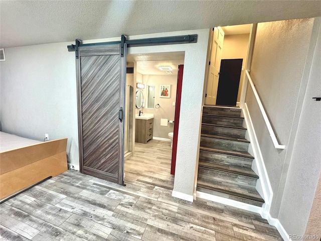 3818 S Dallas St, Aurora, CO 80014 - stairway with wood finished floors, a barn door, a textured wall, baseboards, and a textured ceiling
