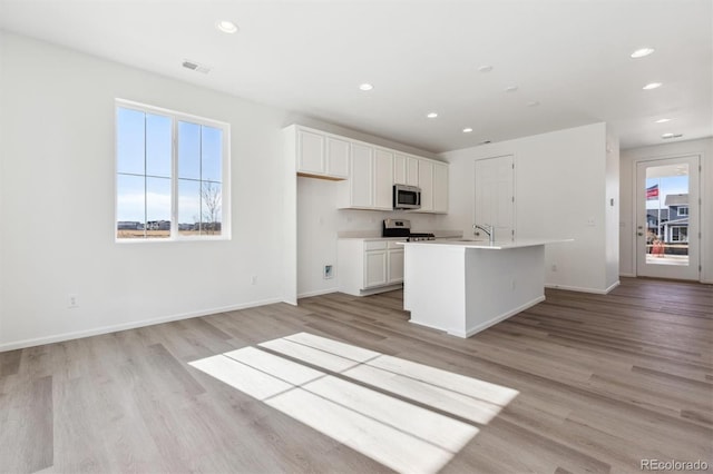 kitchen with sink, a center island with sink, appliances with stainless steel finishes, light hardwood / wood-style floors, and white cabinets