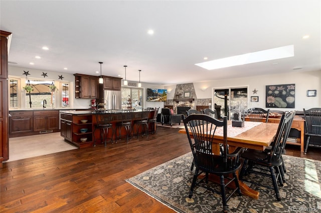 dining room with recessed lighting, wood finished floors, a skylight, and a stone fireplace