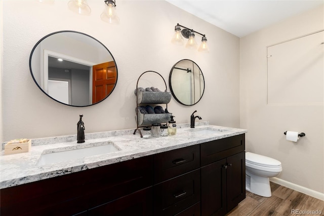 bathroom featuring double vanity, wood finished floors, toilet, and a sink