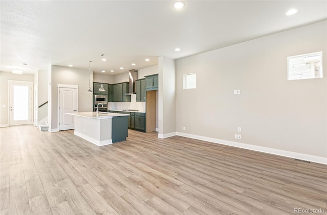 kitchen with sink, wall chimney exhaust hood, light hardwood / wood-style flooring, an island with sink, and pendant lighting