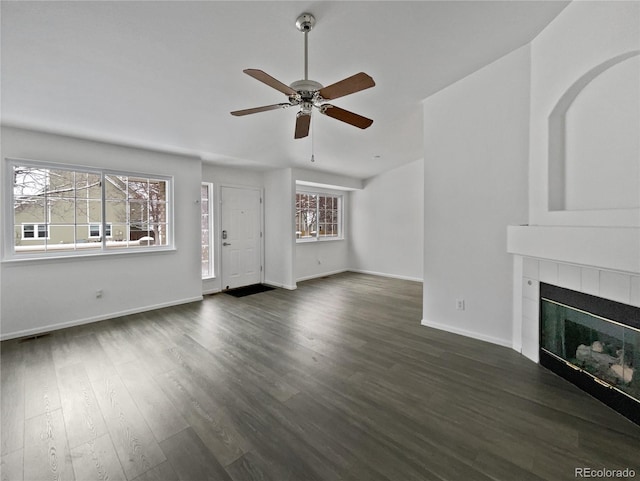 unfurnished living room featuring a tile fireplace, a wealth of natural light, dark wood-type flooring, and ceiling fan