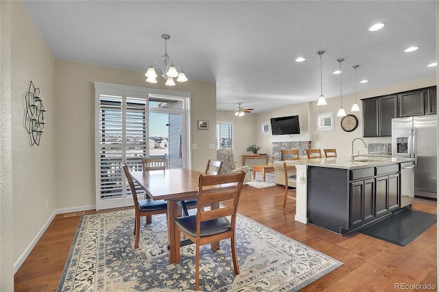 dining space featuring hardwood / wood-style floors, ceiling fan with notable chandelier, a fireplace, and sink