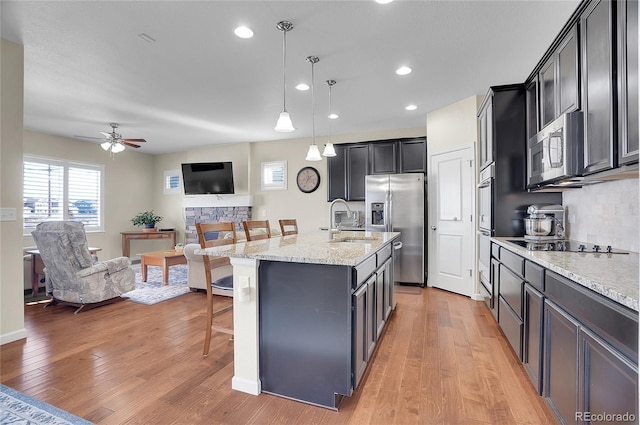 kitchen with sink, a breakfast bar, appliances with stainless steel finishes, a kitchen island with sink, and hanging light fixtures