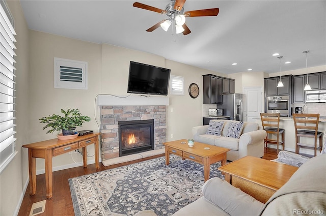 living room featuring dark wood-type flooring, ceiling fan, and a brick fireplace