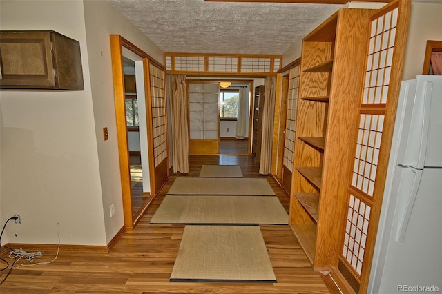 hall with light wood-type flooring, french doors, and a textured ceiling