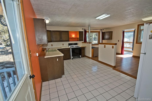 kitchen featuring dark brown cabinetry, gas stove, white refrigerator, sink, and light tile patterned floors