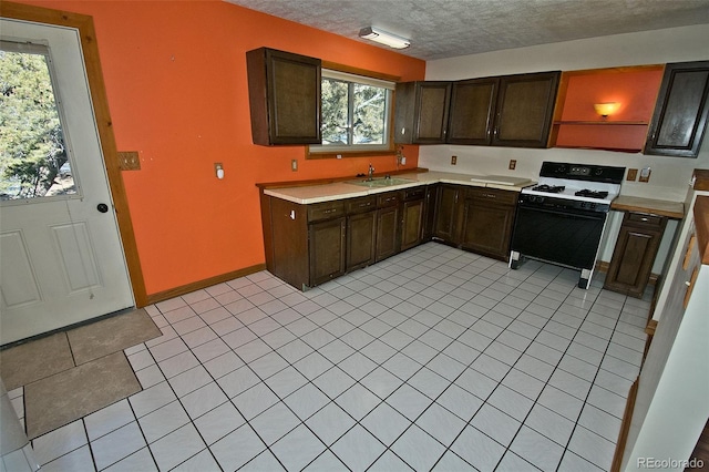 kitchen with a textured ceiling, gas stove, dark brown cabinetry, and sink