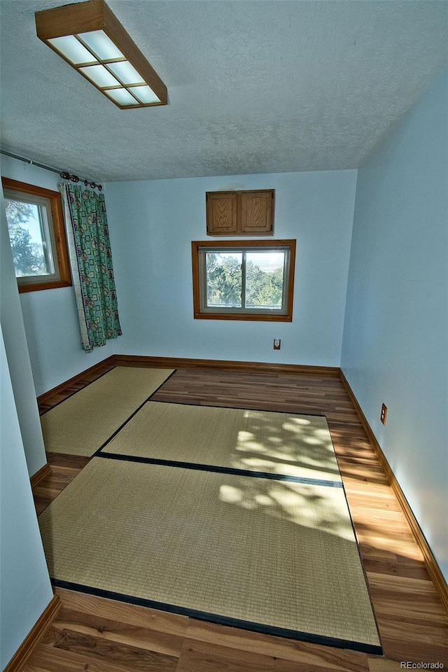 unfurnished room featuring a textured ceiling, dark wood-type flooring, and a wealth of natural light