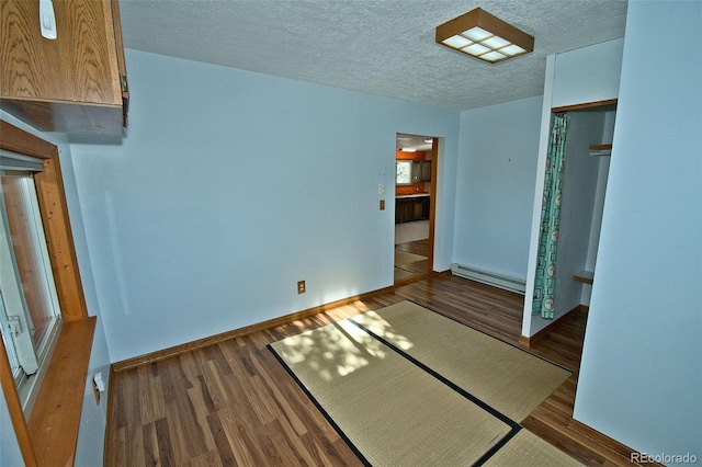 empty room featuring a baseboard heating unit, dark wood-type flooring, and a textured ceiling