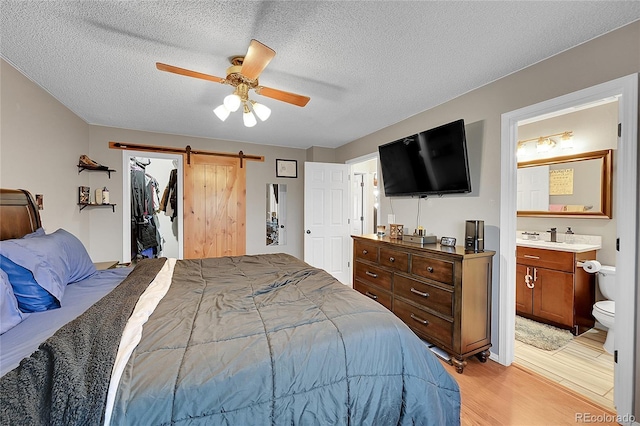 bedroom with a walk in closet, ceiling fan, connected bathroom, light hardwood / wood-style floors, and a closet