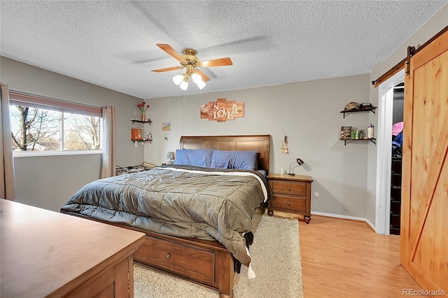 bedroom featuring a barn door, ceiling fan, light hardwood / wood-style flooring, and a textured ceiling