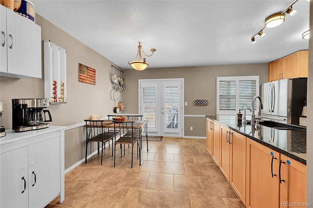 kitchen featuring pendant lighting, dark stone counters, french doors, sink, and stainless steel refrigerator