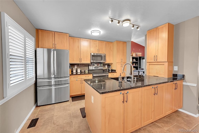 kitchen featuring dark stone counters, kitchen peninsula, light brown cabinetry, and stainless steel appliances