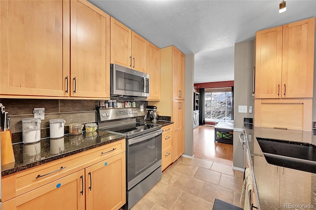 kitchen featuring dark stone countertops, light brown cabinetry, light tile patterned floors, and stainless steel appliances