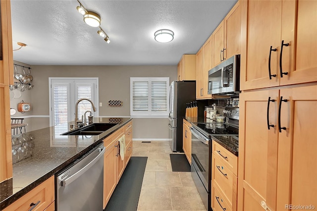 kitchen with appliances with stainless steel finishes, light brown cabinets, dark stone counters, and sink