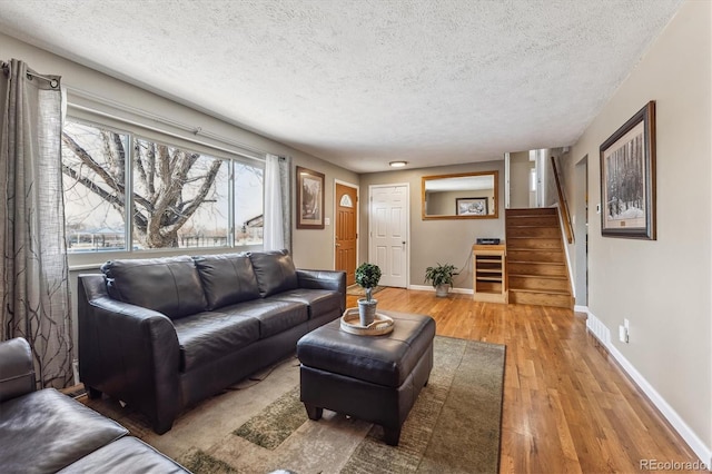 living room with light wood-style flooring, a textured ceiling, stairway, and baseboards