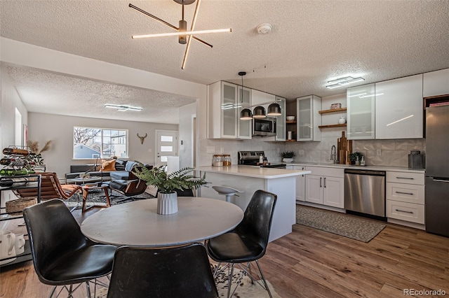 kitchen with wood-type flooring, white cabinetry, appliances with stainless steel finishes, and pendant lighting