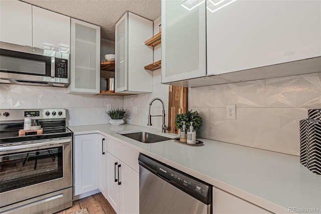 kitchen featuring appliances with stainless steel finishes, light wood-type flooring, backsplash, sink, and white cabinetry