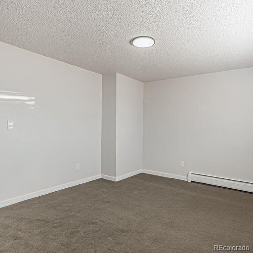 spare room featuring dark carpet, a textured ceiling, and baseboard heating