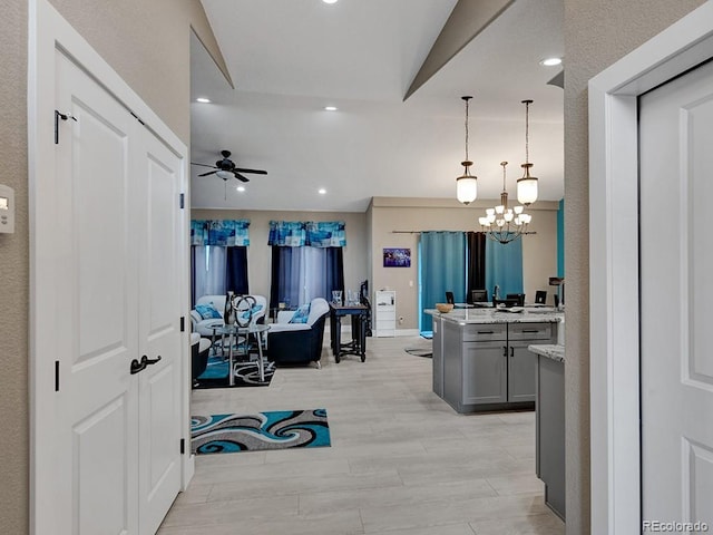 interior space with pendant lighting, lofted ceiling, gray cabinets, light hardwood / wood-style flooring, and ceiling fan with notable chandelier