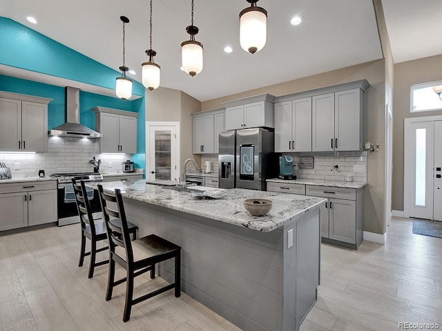 kitchen featuring hanging light fixtures, an island with sink, wall chimney exhaust hood, and appliances with stainless steel finishes