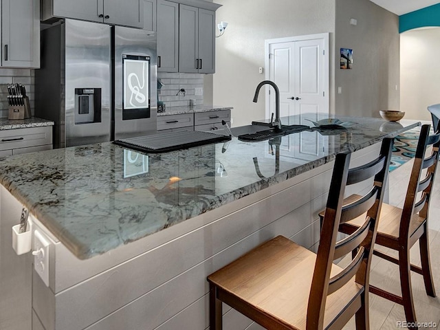 kitchen featuring light stone counters, a spacious island, stainless steel fridge, and gray cabinetry