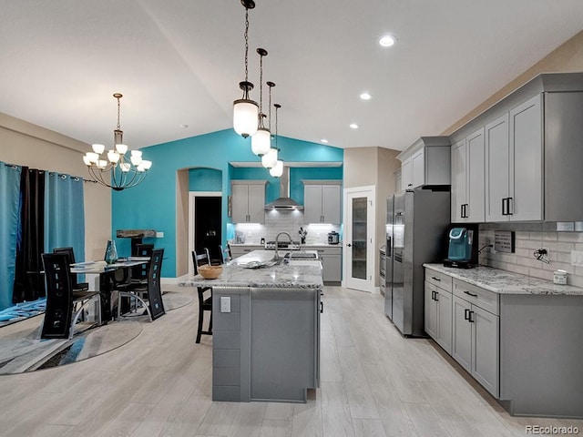 kitchen with pendant lighting, a kitchen island with sink, wall chimney range hood, and stainless steel fridge with ice dispenser