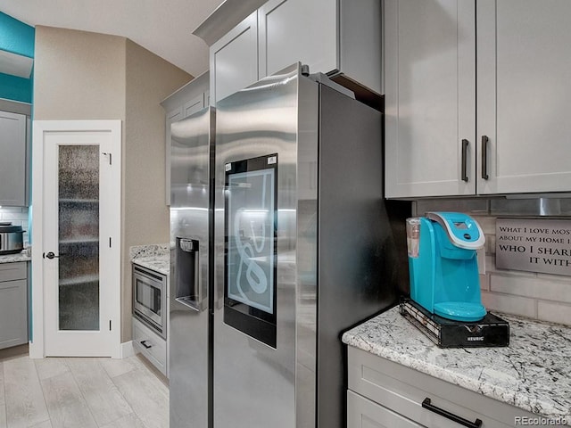 kitchen featuring stainless steel appliances, light stone countertops, gray cabinetry, and backsplash