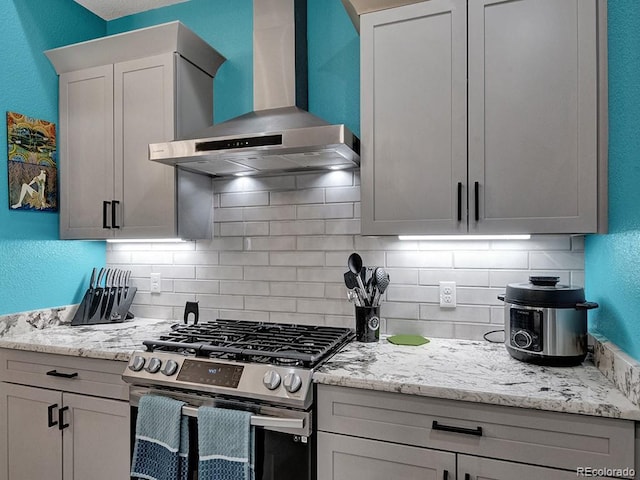 kitchen with light stone countertops, stainless steel gas range, backsplash, and wall chimney exhaust hood