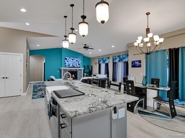 kitchen featuring ceiling fan with notable chandelier, lofted ceiling, decorative light fixtures, and an island with sink