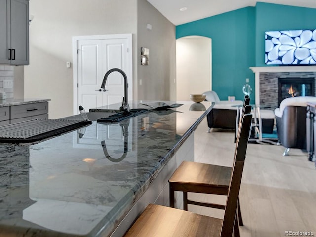 kitchen with lofted ceiling, gray cabinets, and stone counters