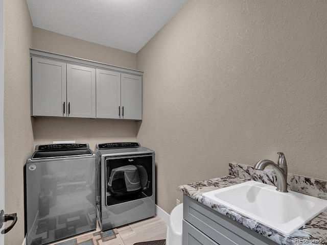 laundry area featuring washer and dryer, sink, light wood-type flooring, cabinets, and a textured ceiling