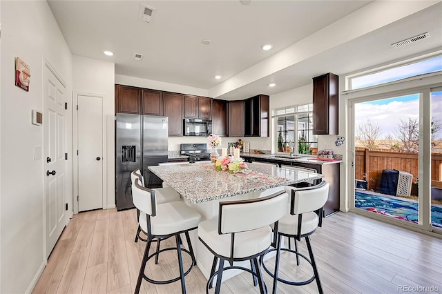 kitchen featuring black appliances, a center island, sink, light hardwood / wood-style flooring, and a breakfast bar area