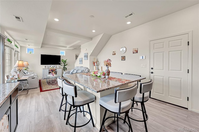 kitchen with a kitchen bar, light stone countertops, light hardwood / wood-style flooring, and a kitchen island