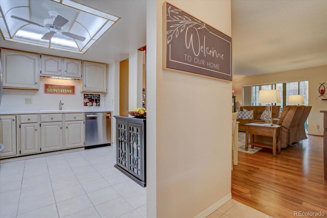 kitchen featuring sink, dishwasher, light tile patterned flooring, ceiling fan, and a skylight