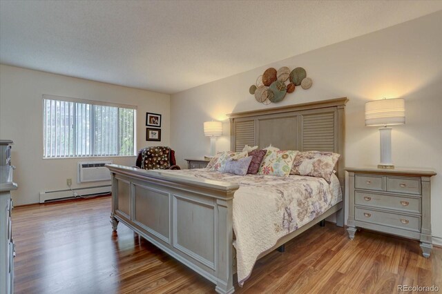 bedroom with baseboard heating, a textured ceiling, a wall mounted AC, and wood-type flooring