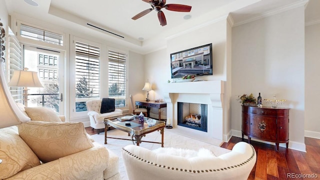 living room featuring baseboards, a lit fireplace, ornamental molding, wood finished floors, and a ceiling fan