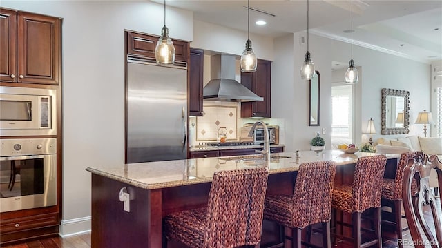 kitchen with light stone counters, dark wood-style floors, wall chimney range hood, decorative backsplash, and built in appliances